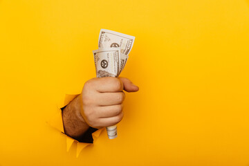 Hand holding crumpled money through hole in yellow paper wall