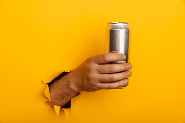 Hand holds metal jar in torn hole of yellow paper wall