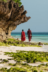 Zanzibar, Tanzania, Nungwi. Detail of the rocky bottom of the beach with two Masai walking.