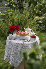 Garden and still life. Tea party in the garden - tart with strawberries and cream, a vase with garden roses and a tea set on the table.