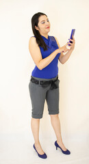 Naklejka premium beautiful, successful, business woman in gray shorts and blue blouse, in purple heels, standing checking earrings on cell phone, on white background