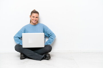 Young woman with a laptop sitting on the floor laughing
