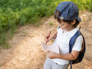 Mindful boy writes something in notebook while walking in forest. Exploring nature.  Summer outdoor recreation. Healthy lifestyle.