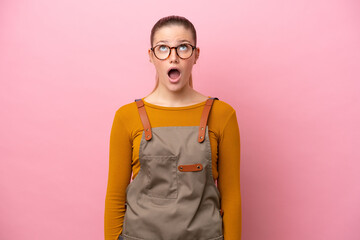 Woman with apron isolated on pink background looking up and with surprised expression