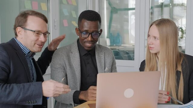 Diverse team of students, young business partners discuss their startup project, supporting each other, caucasian man pat on the shoulder his african black colleague. Meeting room in office