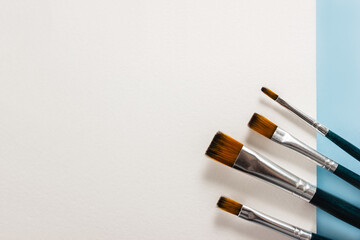 Paint brushes on white canvas and blue background. Selective focus, copy space