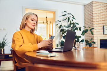 Mid adult woman using phone while sitting at table working from home