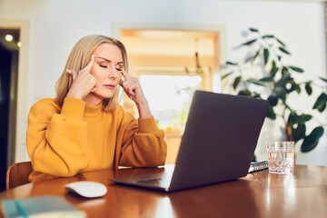 Stressed young woman sitting with closed eyes at from of laptop while working at home office