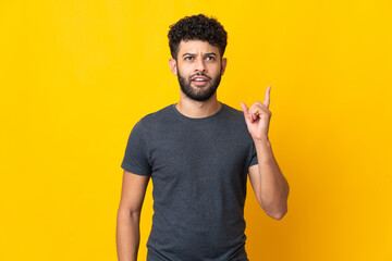 Fototapeta premium Young Moroccan man isolated on yellow background thinking an idea pointing the finger up