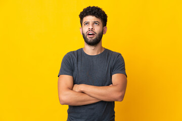 Young Moroccan man isolated on yellow background looking up and with surprised expression