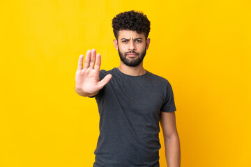 Young Moroccan man isolated on yellow background making stop gesture