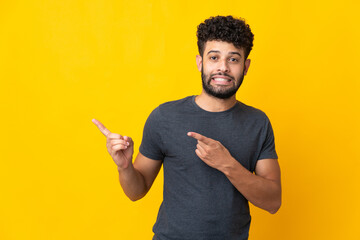 Young Moroccan man isolated on yellow background frightened and pointing to the side