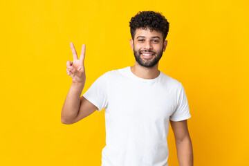 Naklejka premium Young Moroccan man isolated on yellow background smiling and showing victory sign
