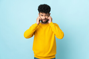 Young Moroccan man isolated on blue background frustrated and covering ears