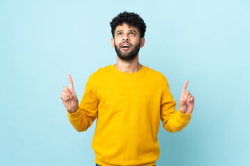 Young Moroccan man isolated on blue background surprised and pointing up