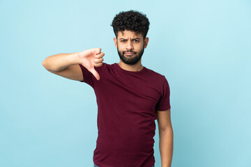 Young Moroccan man isolated on blue background showing thumb down with negative expression