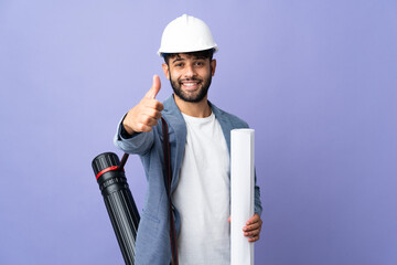 Young architect Moroccan man with helmet and holding blueprints over isolated background with...