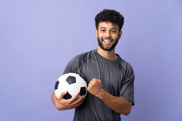 Handsome Moroccan young football player man over isolated on purple background celebrating a victory