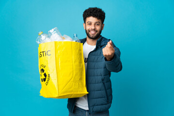 Young Moroccan man holding a bag full of plastic bottles to recycle over isolated background making...