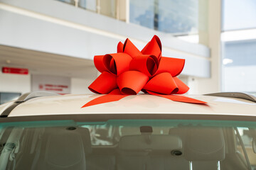 a red gift bow on the roof of a new white car in the car dealership. 