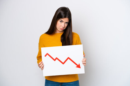 Young Brazilian woman isolated on white background holding a sign with a decreasing statistics arrow symbol with sad expression