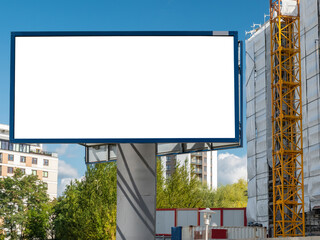 Blank white billboard for advertisement in front of the construciton site. Residential area on the sunny summer day.