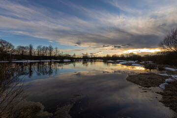 Epic spring landscape by the river. The flood of the river in early spring. A colorful sunset is reflected in the water. March evening landscape.