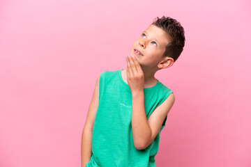 Little caucasian boy isolated on pink background looking up while smiling