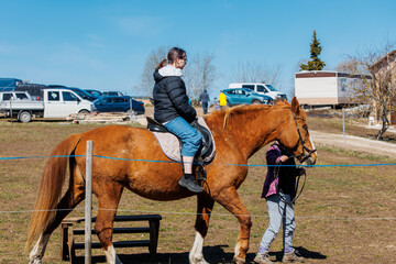 A girl learns to ride a horse with a trainer on an eco-farm