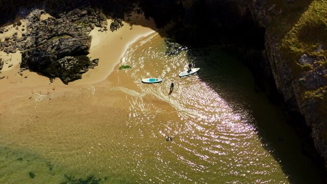 2 men with paddle boards waiting for friends to come through cave at three cliff bay swansea south wales uk.