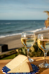 Spanish hard manchego, cow, sheep and goat cheese served outdoor with glasses of white wine and view on blue sea
