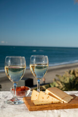 Spanish hard Andalusian cheese filled with sweet sherry served outdoor with membrillo jam with two glasses of white wine with beach and blue sea on background