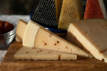 Assortment of Spanish hard cheeses, curado, manchego, goat cheese served outdoor with membrillo jam with blue sea on background