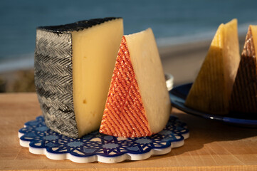 Assortment of Spanish hard cheeses, curado, manchego, goat cheese served outdoor with membrillo jam on andalusian style blue board with blue sea on background