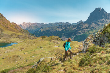 Fototapeta na wymiar Young Attractive Woman With A Backpack hiking in a beautiful valley between mountains during the sunset. Discovery Travel Destination Concept