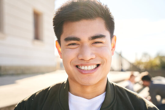 Outdoor portrait of a smiling Chinese guy looking at the camera laughing with positive face and friendly look. Close up of a Happy human face - Cheerful Asian young man. People and emotions.