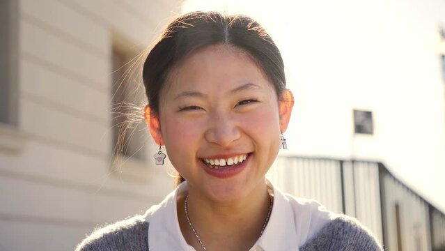 Outdoor portrait of a smiling Chinese girl looking at the camera laughing with positive face and friendly look. Close up of a Happy human face - Cheerful Asian girl. Concept of people and emotions.