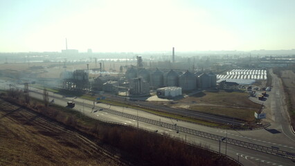 Fototapeta premium Landscape Grain Elevator. Aerial Drone View. Flight Over Metal Round Silos for Grain Storage and Grain-drying complex outdoors. Highway and driving cars. Harvesting, processing, storage elevator