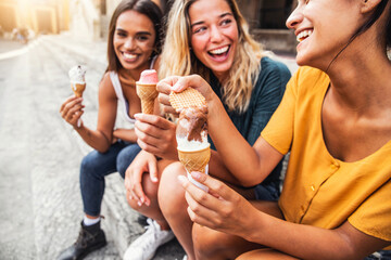 Laughing teenage girls eating ice cream cones on city street - Young female friends enjoying...