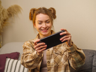 Cheerful girl gamer plays a video game on a portable game console in the room. Cyberspace, cybersport, communication with friends, fun competitions, leisure, game strategy. - 503210146