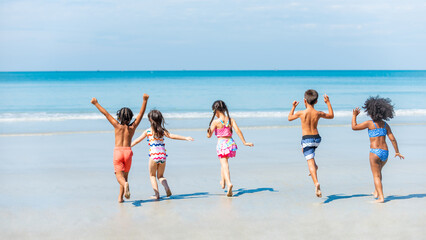 Group of Diversity little child boy and girl friends running and playing in sea water on tropical beach together on summer vacation. Happy children kid enjoy and fun outdoor lifestyle on beach holiday