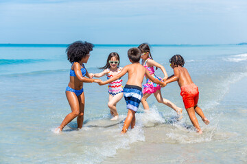 Group of Diversity little child boy and girl friends running and playing in sea water on tropical beach together on summer vacation. Happy children kid enjoy and fun outdoor lifestyle on beach holiday