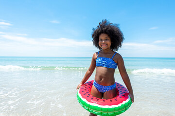 Portrait of Smiling African child girl in swimwear and swim ring playing on tropical beach in...