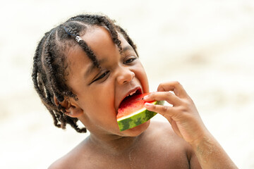 Little African child boy in swimwear eating watermelon while playing with family on tropical beach...