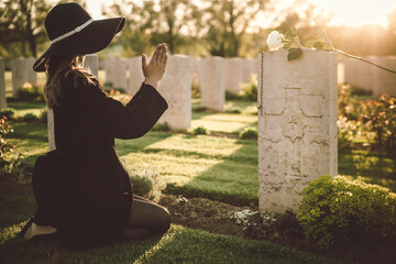 Sad woman in the cemetery praying on tombstone - Female grieving for a lost love - Religion and...