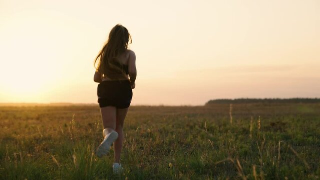 Free young woman runs in summer park at sunset. Running after sun. Training jogging. Healthy beautiful girl is engaged in fitness, jogging in country in sun. Jogger girl breathes fresh air on field.