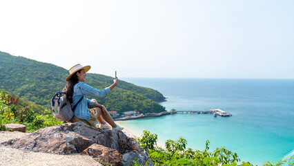 Young Asian woman traveler using mobile phone taking selfie while solo travel on tropical island...