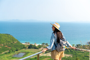 Young beautiful Asian woman with backpack solo travel on tropical island mountain peak in summer...