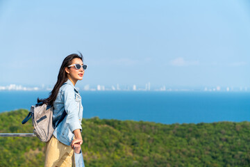 Young beautiful Asian woman with backpack solo travel on tropical island mountain peak in summer...