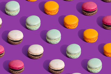 Fototapeta premium Colorful macarons ona dark purple background. Summer pattern of sweet food. Aesthetic still life concept. Trendy colors with strong contrast.